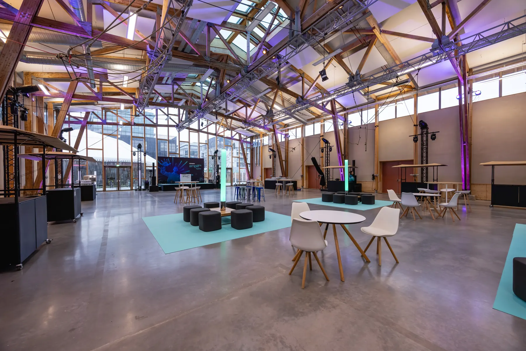 Grand hall événementiel sous charpente bois, mobilier et éclairages prêts à accueillir un événement