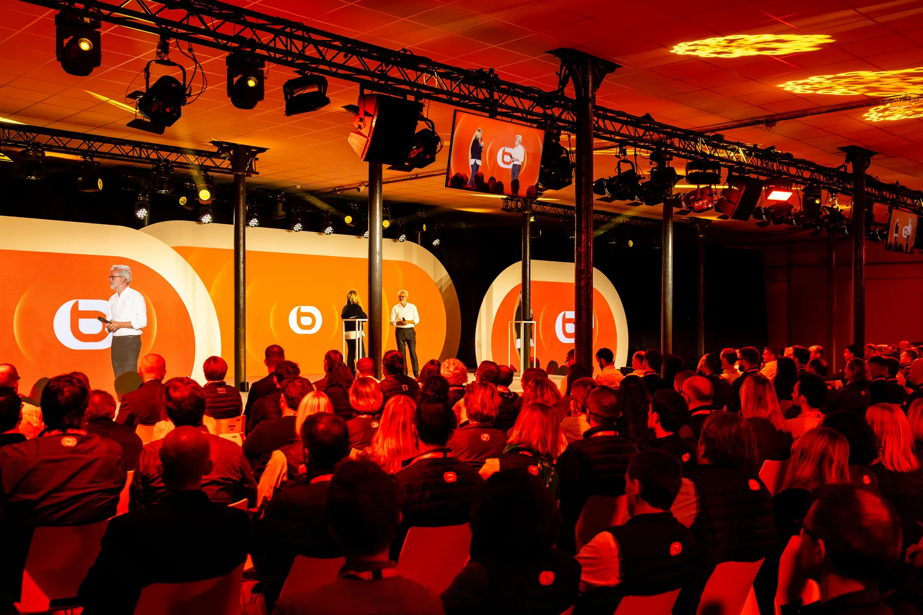 Salle comble sous des lumières rouges face à la scène d’une convention d’entreprise
