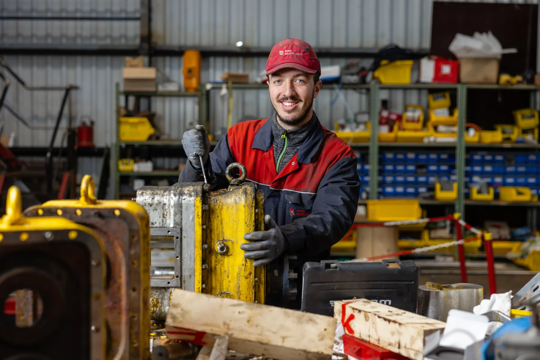 Technicien souriant dans un atelier de maintenance, pièces mécaniques au premier plan