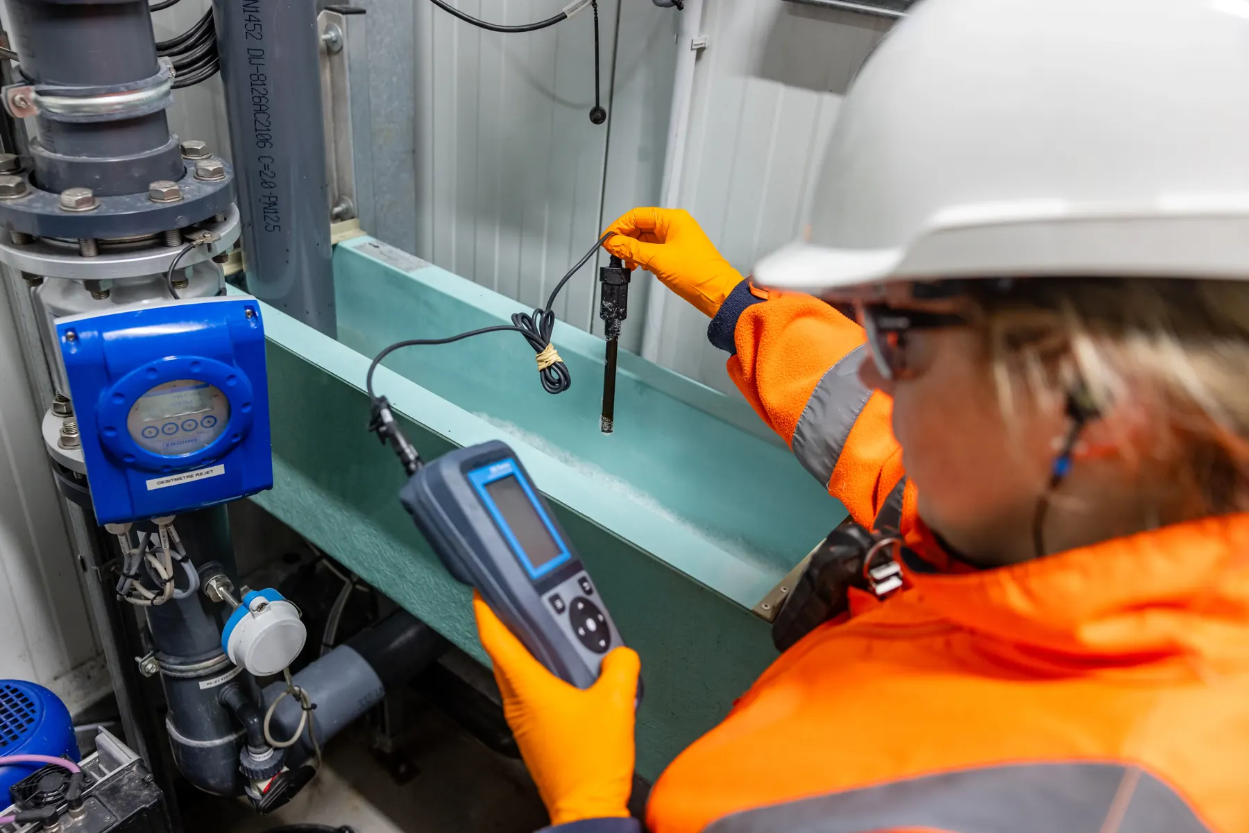 Technicienne en EPI effectuant une mesure avec un appareil portable sur une installation technique