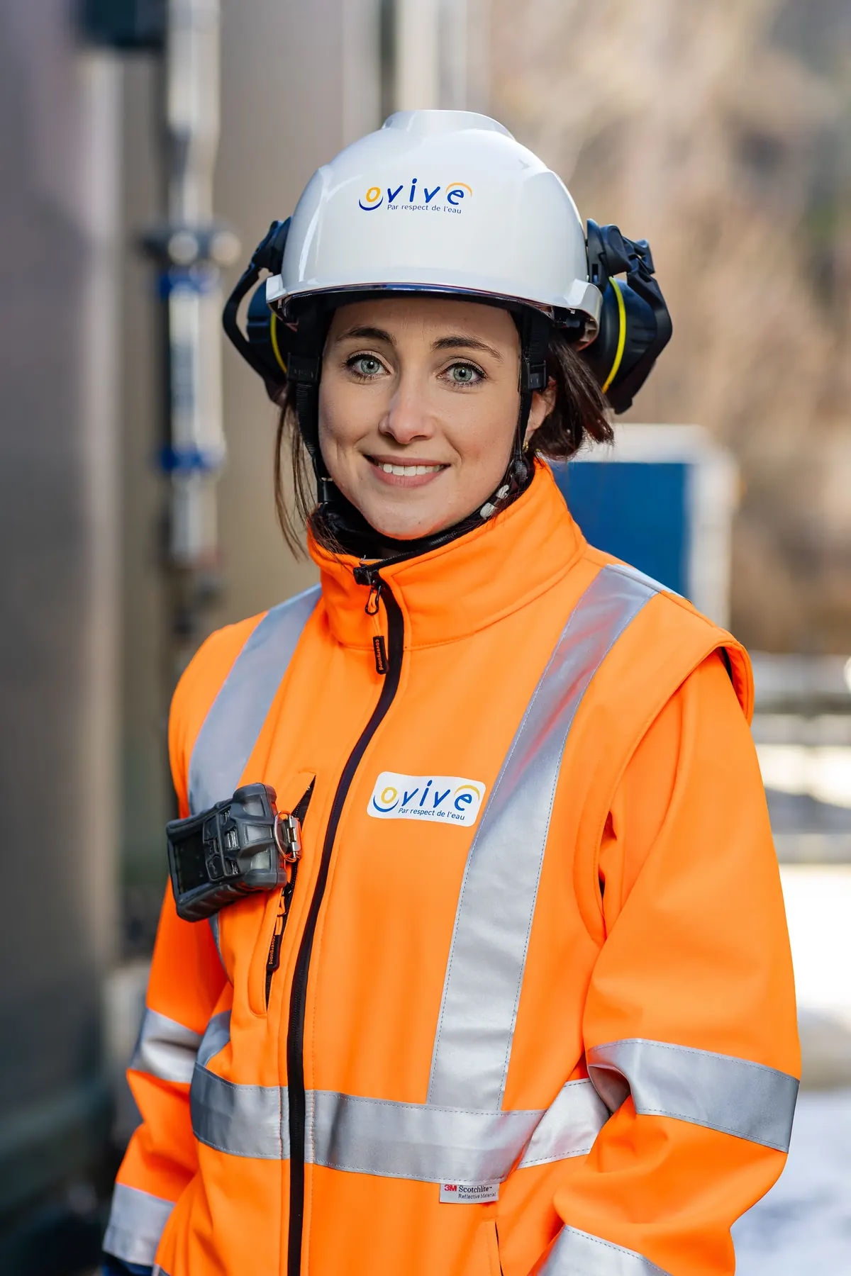 Portrait d’une technicienne souriante en casque et veste haute visibilité sur site industriel
