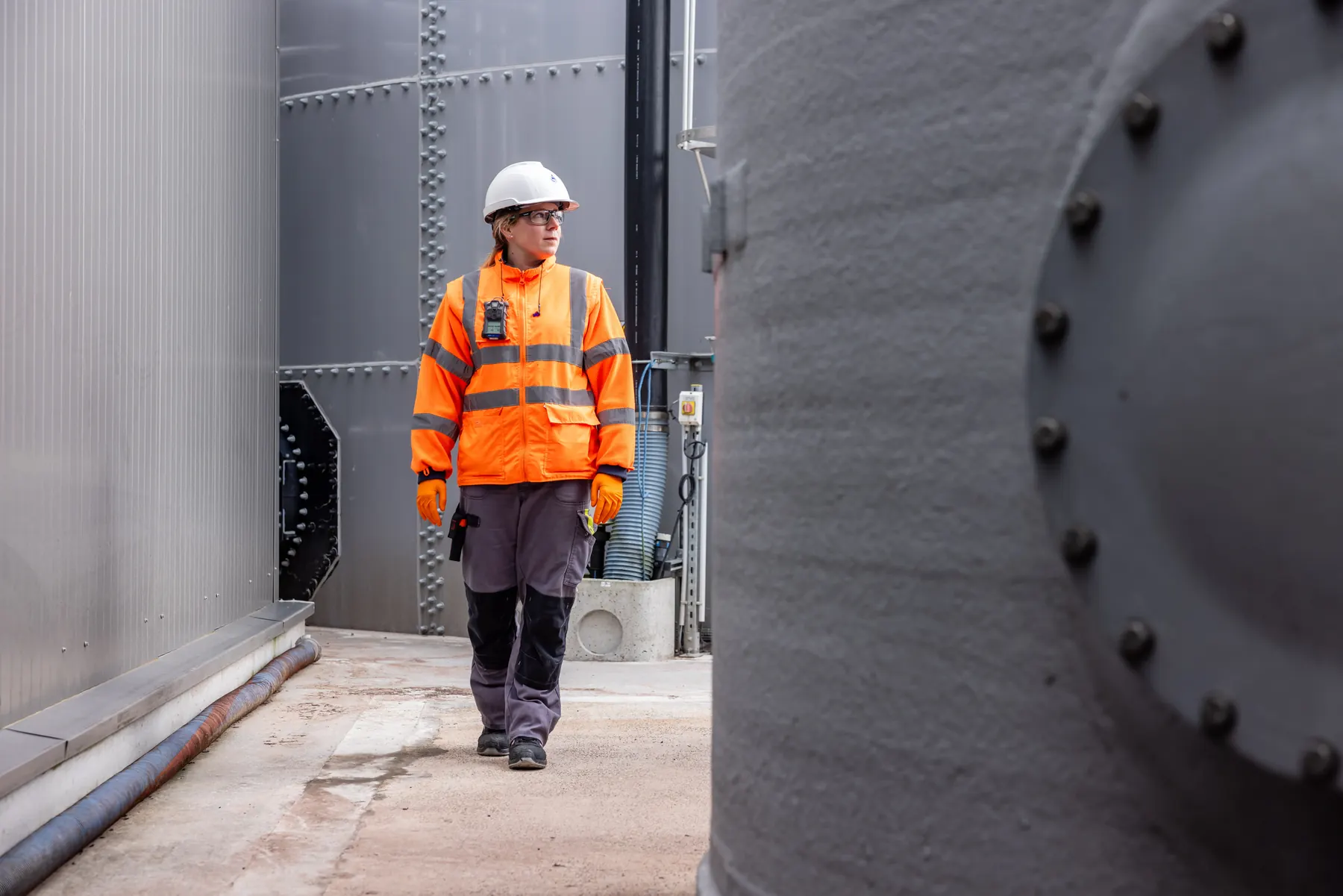 Technicien en EPI marchant entre de grandes cuves industrielles