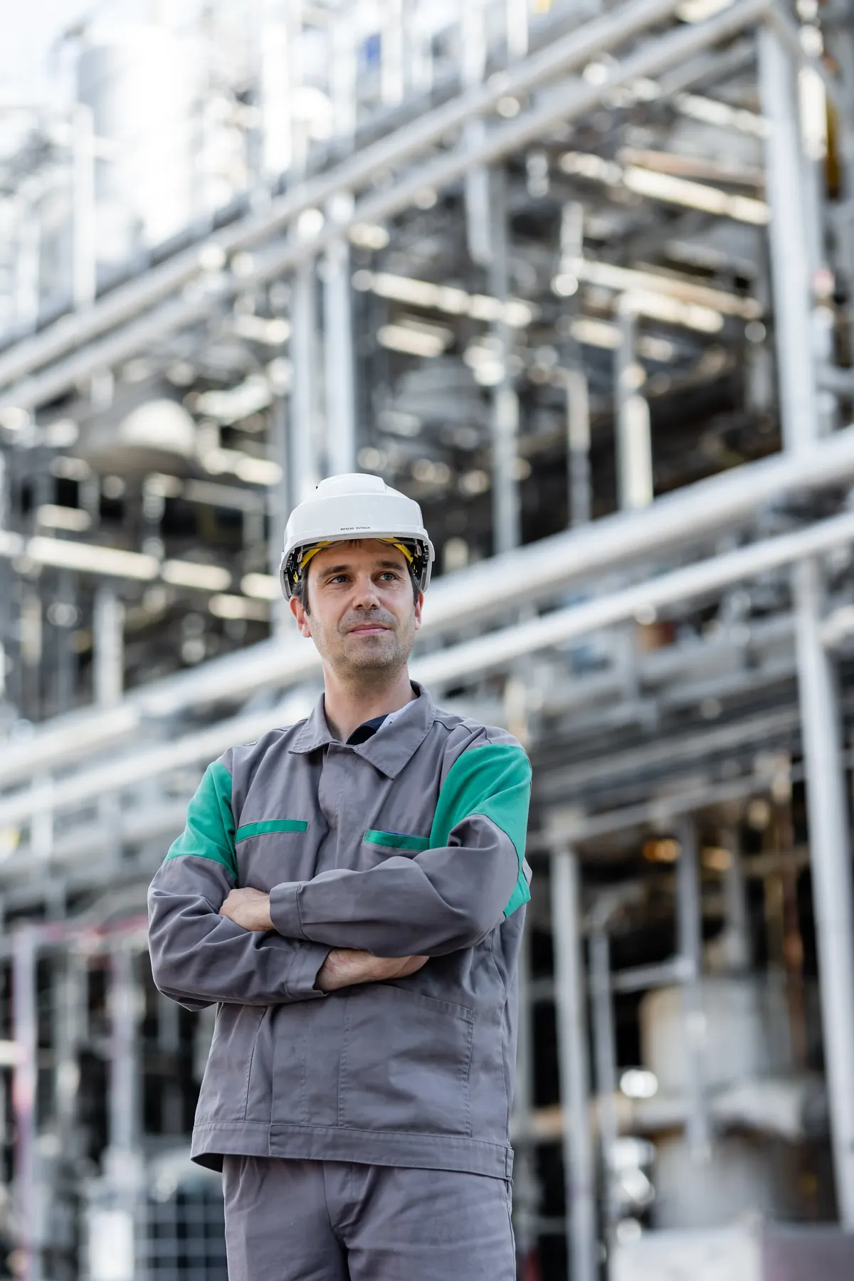 Responsable de site en tenue de travail et casque, bras croisés devant les installations industrielles